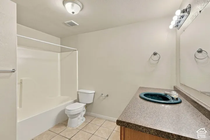 Integrated bathtub and shower combination, tiled flooring, vanity with countertop, wall-mounted mirror, and overhead vanity lighting