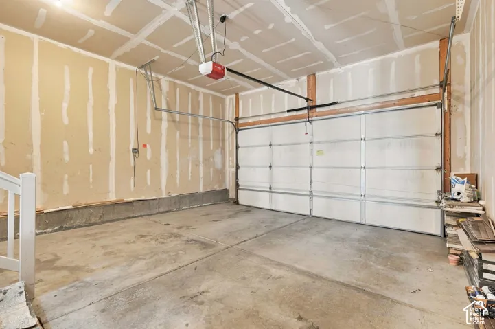 Concrete flooring, white paneled garage door, exposed ceiling joists, and a garage door opener system