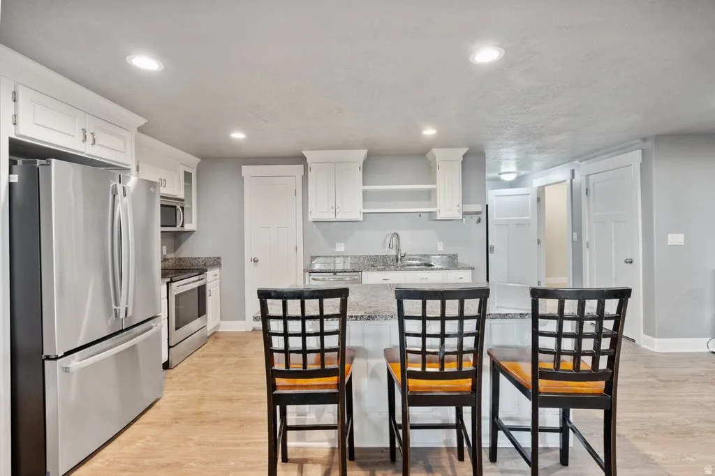 Contemporary kitchen featuring white cabinetry, stainless steel appliances, granite countertops, an island with seating, and recessed lighting