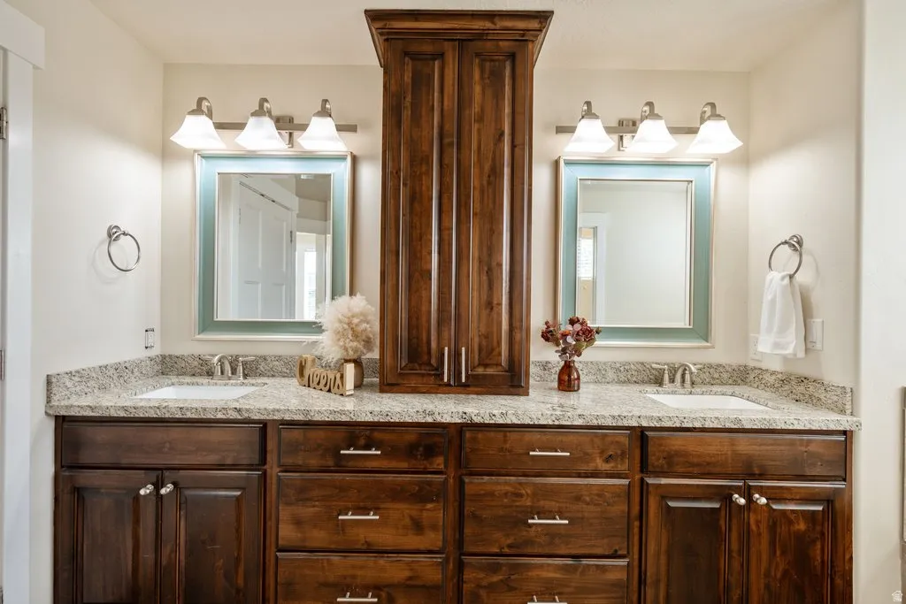 Dual sink vanity with granite-style countertop, undermount sinks, wood cabinetry, and brushed nickel fixtures