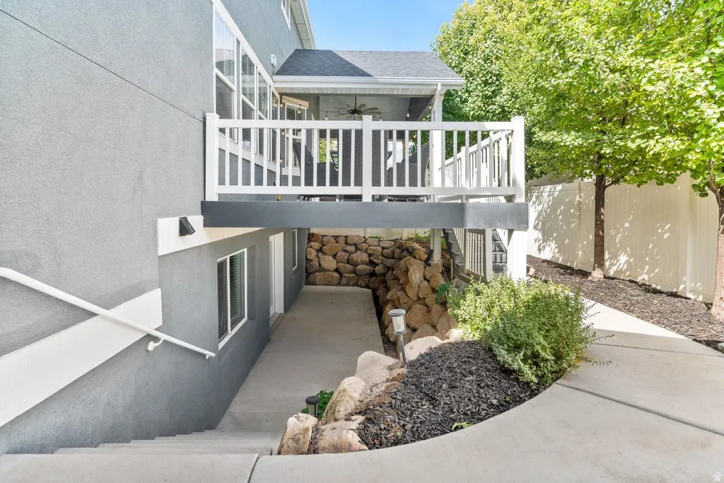 Covered outdoor deck with white railing, concrete stairway, and lower level entry