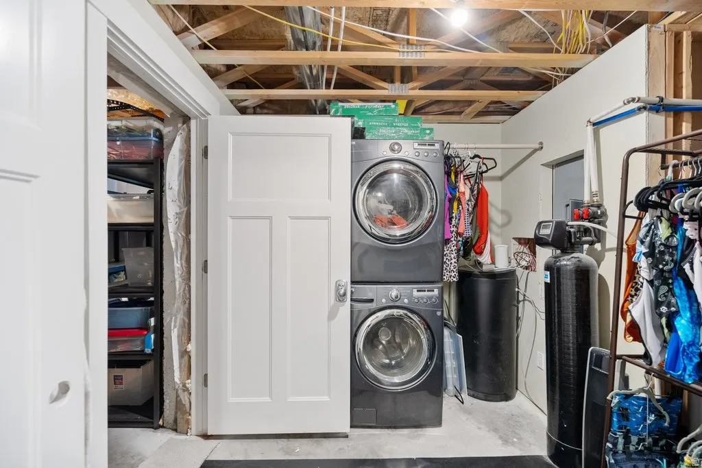 Laundry area with stacked washing machine and dryer, exposed ceiling joists, and water filtration system
