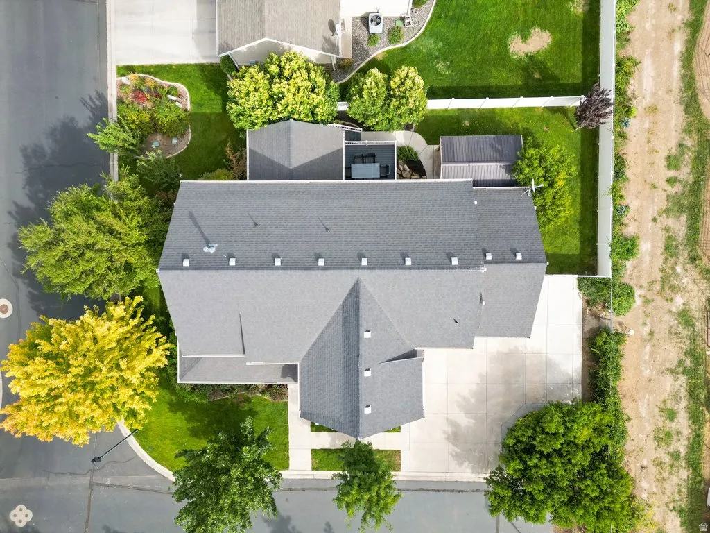 Asphalt shingle roof, paved driveway, landscaped yard with mature trees, privacy fencing, and additional outbuilding