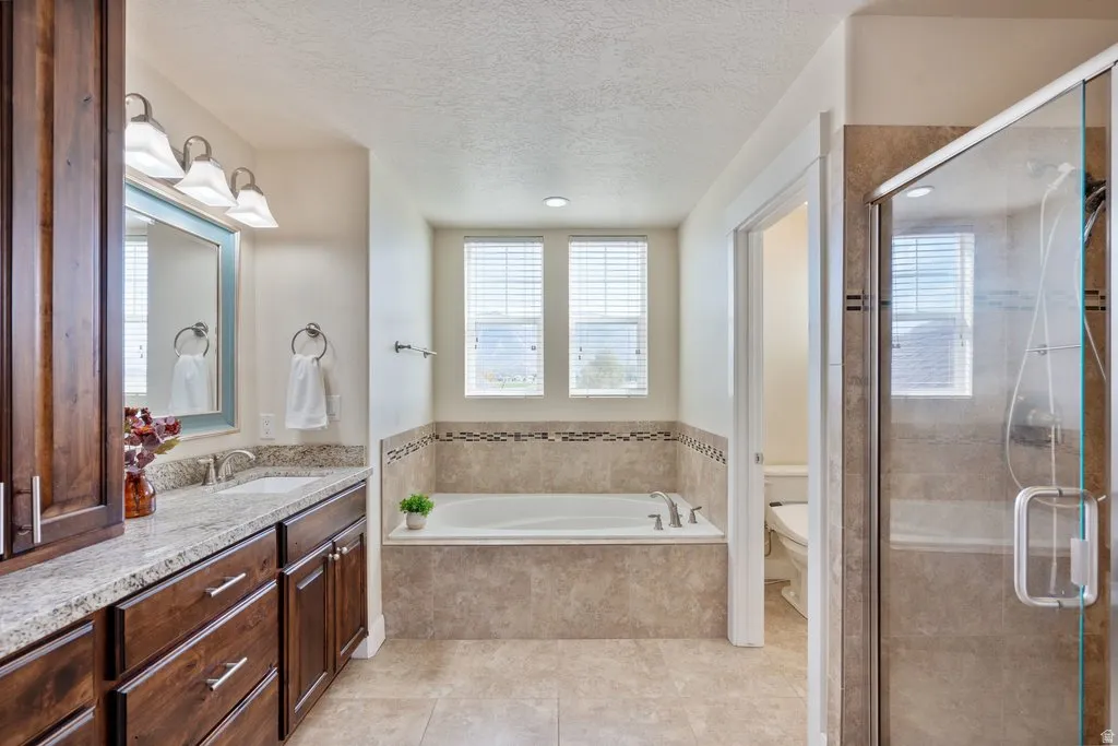 Spacious bathroom featuring a built-in soaking tub, a separate glass-enclosed shower, dual vanity with a granite countertop, and wood-finish cabinetry