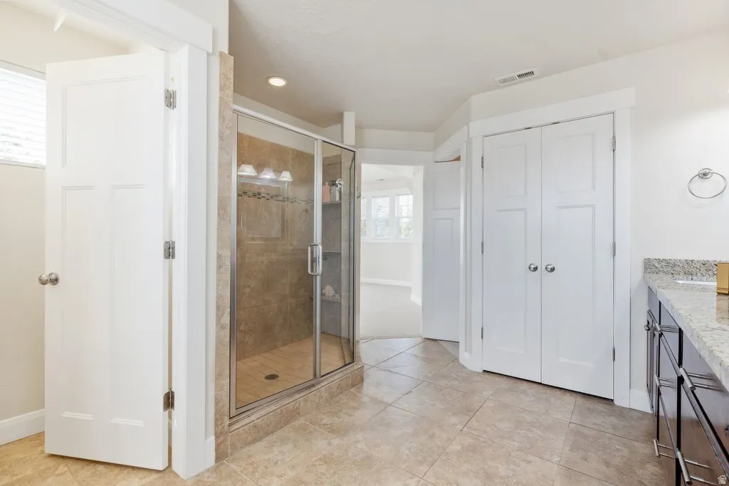 Glass-enclosed shower with tiled surround, light-toned floor tiling, and a vanity with a light-colored countertop