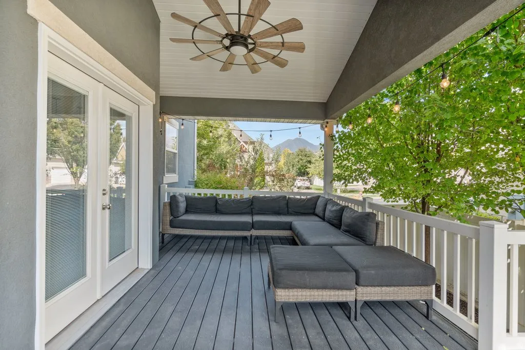 Covered outdoor deck with a ceiling fan, white railings, and mountain backdrop