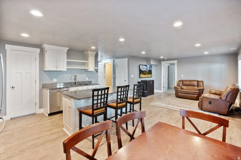 Recessed lighting, wood-finish flooring, white cabinetry, stainless steel dishwasher, and granite countertops