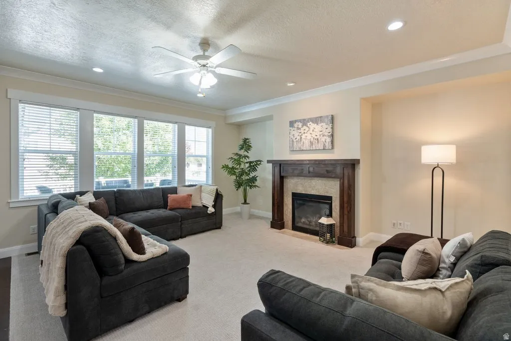 Living area with recessed lighting, crown molding, a ceiling fan, and a fireplace featuring a wood mantel