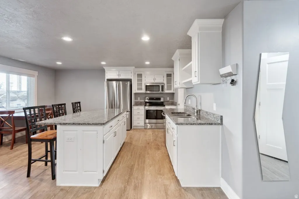 Kitchen featuring white cabinetry, granite-finish countertops, stainless steel appliances, a center island, and wood-finish flooring