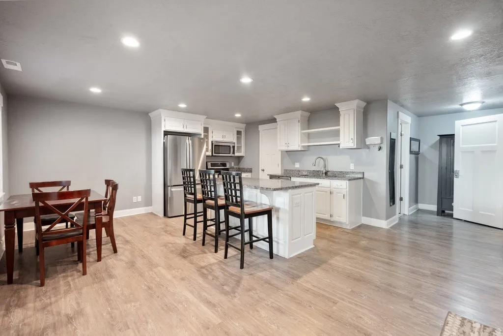 Modern kitchen featuring white cabinetry, stainless steel appliances, granite countertops, and wood-finish flooring