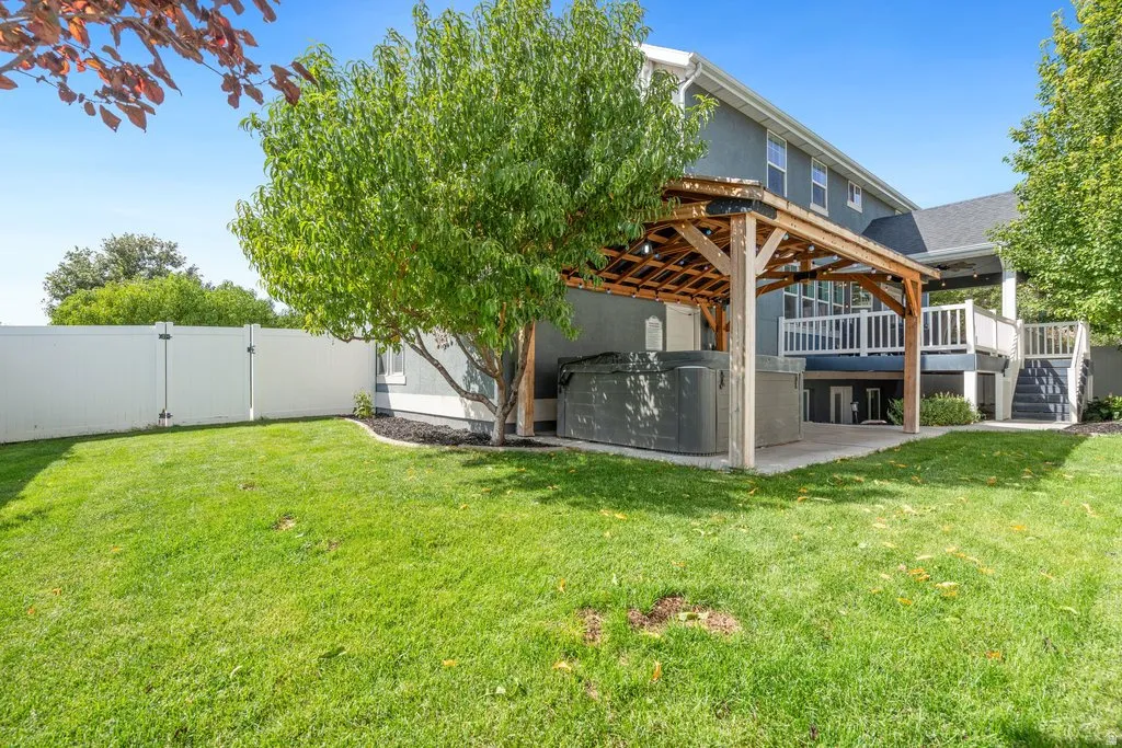 Expansive green lawn, white privacy fence, multi-level deck with white railings, and a covered patio with a built-in spa
