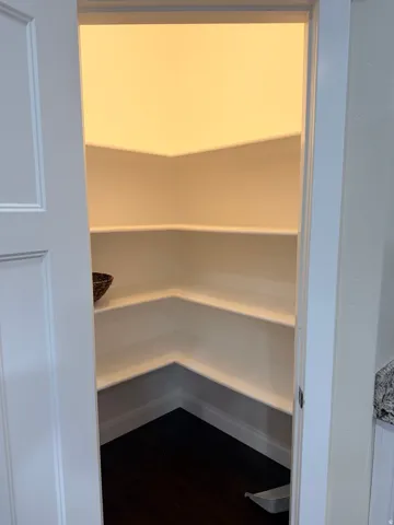 Walk-in pantry featuring multiple white shelves and dark wood-finish flooring