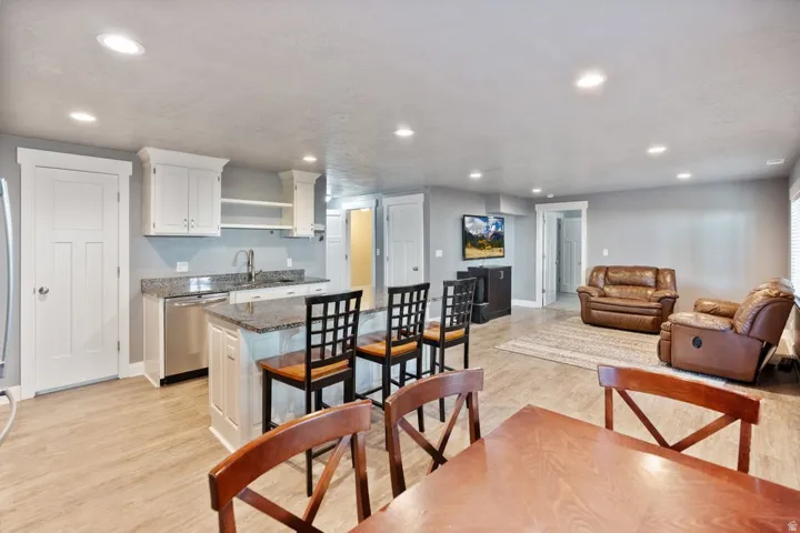 Recessed lighting, wood-finish flooring, white cabinetry, stainless steel dishwasher, and granite countertops