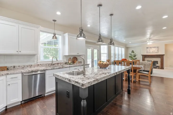 Kitchen featuring wood-finish flooring, white cabinetry, a black kitchen island with a sink, stainless steel appliances, and pendant lighting