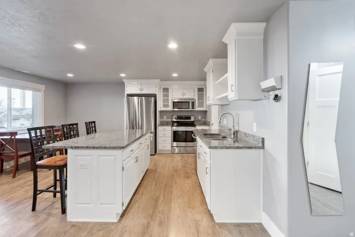 Kitchen featuring white cabinetry, granite-finish countertops, stainless steel appliances, a center island, and wood-finish flooring