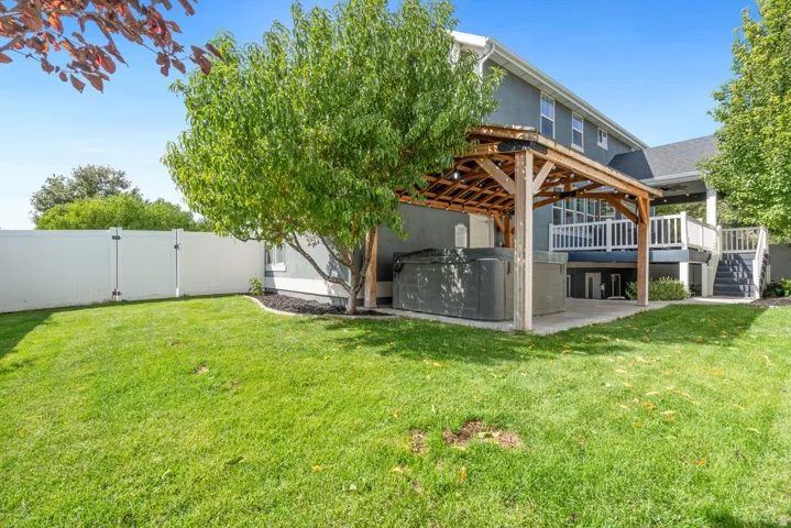 Expansive green lawn, white privacy fence, multi-level deck with white railings, and a covered patio with a built-in spa