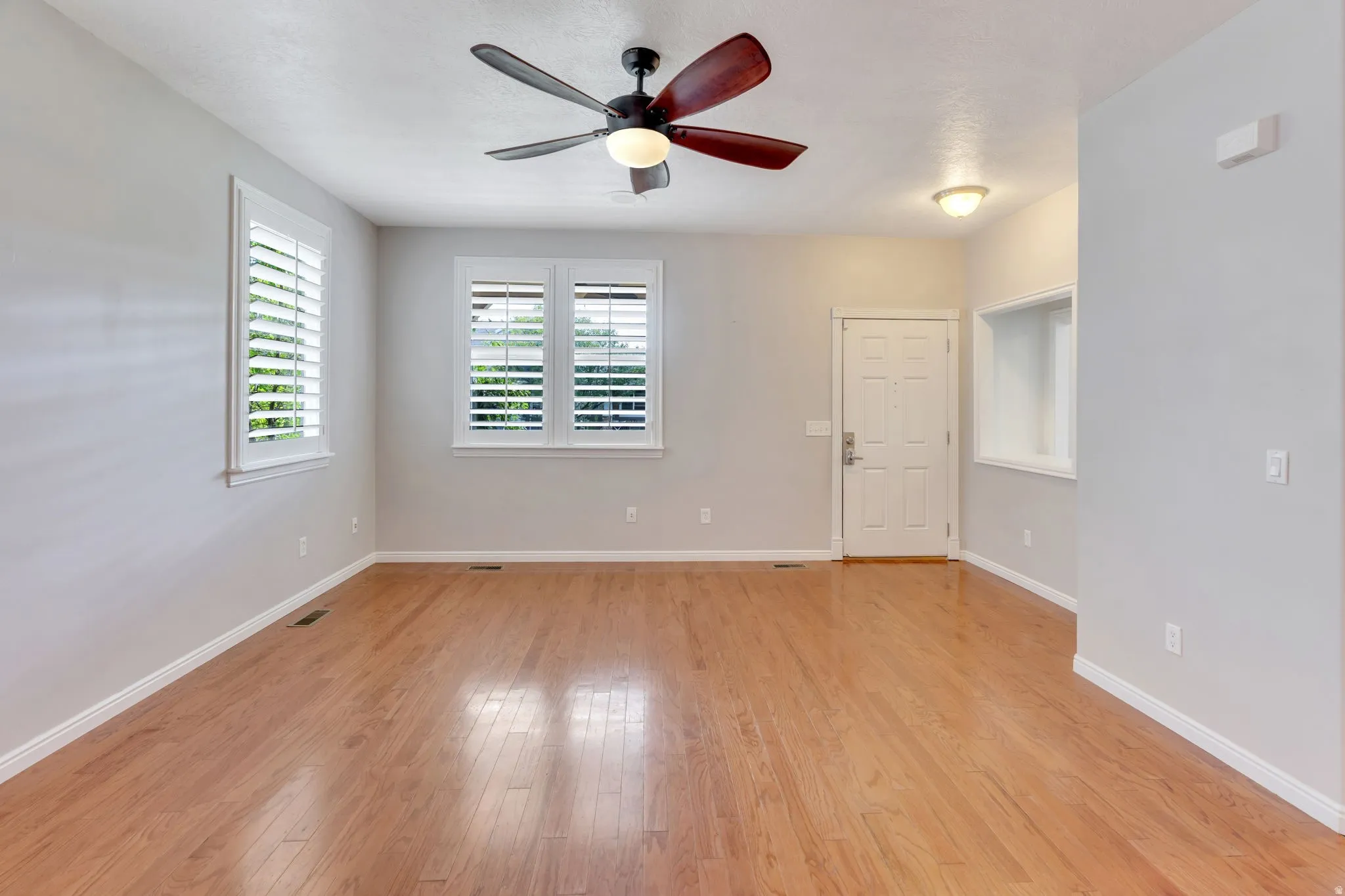 Wood-finish flooring throughout, multiple windows with plantation shutters, ceiling fan with integrated lighting, recessed wall niche, and panel door entry