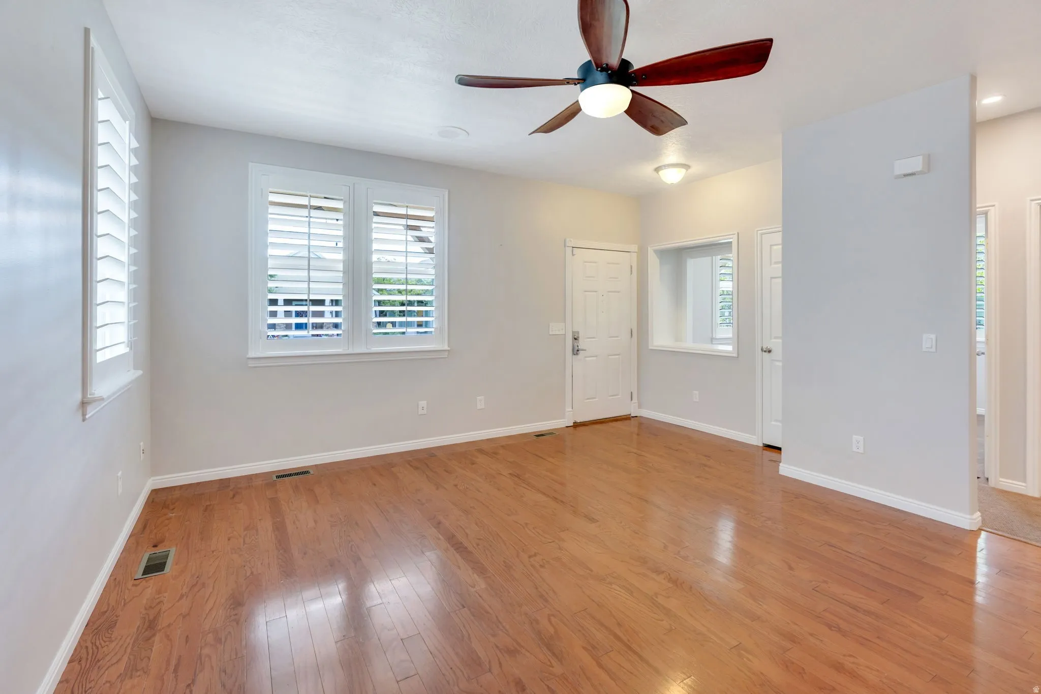 Spacious room featuring wood-finish flooring, white plantation shutters, a ceiling fan with integrated lighting, and recessed ceiling lights