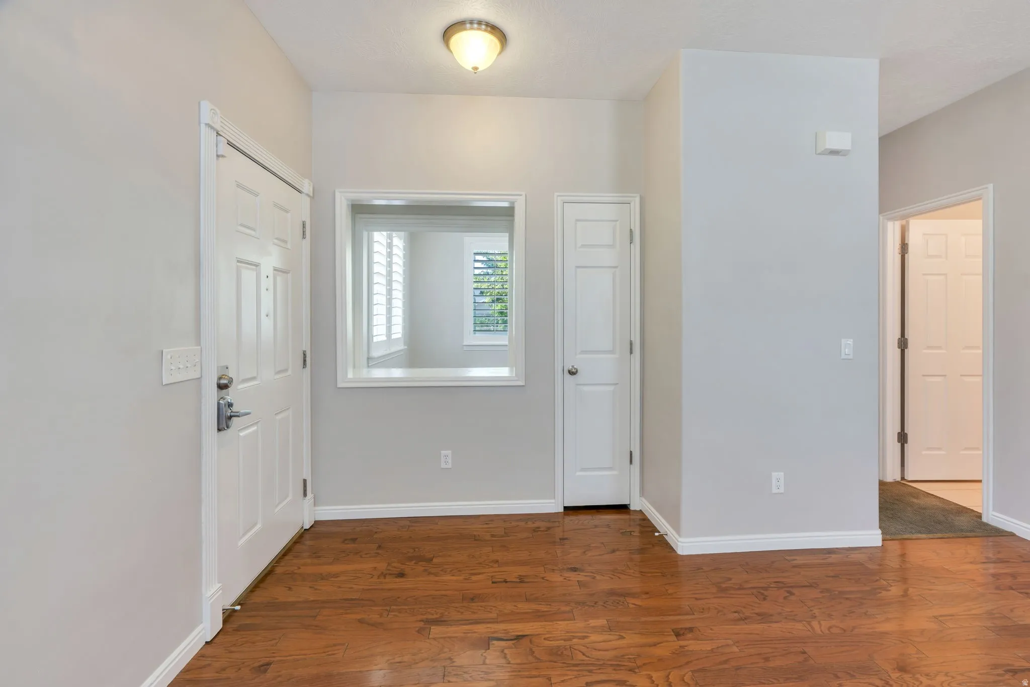 Entryway featuring wood-finish flooring, white paneled doors, and a decorative interior window with plantation shutters
