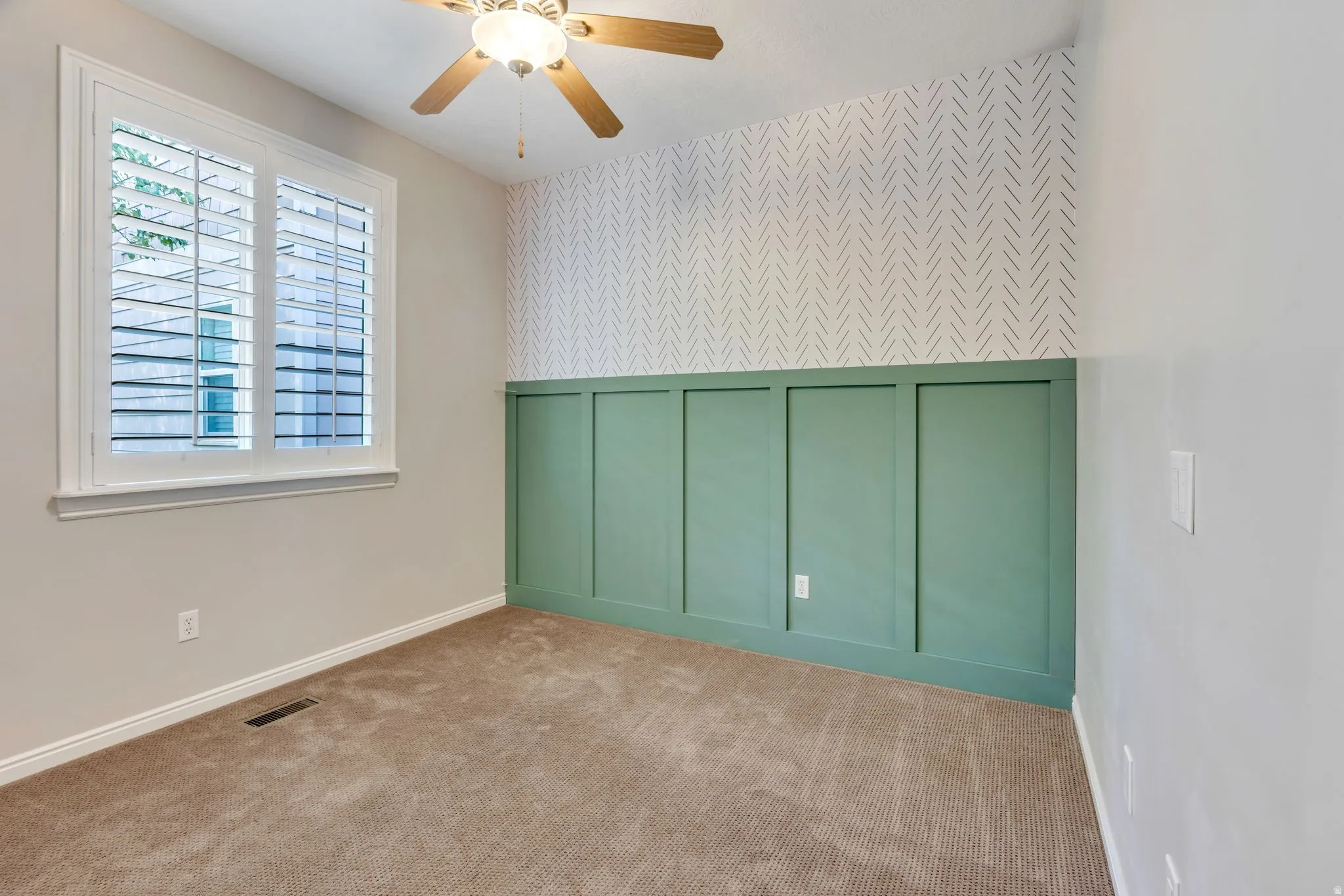 Window with interior plantation shutters, wood-finish ceiling fan, full wall paneling, patterned accent wall, and carpet flooring