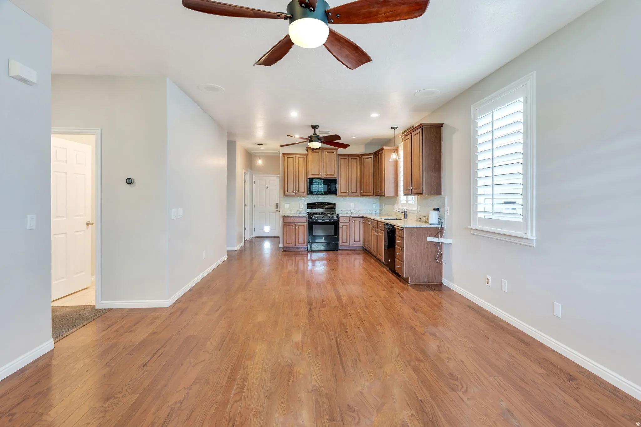 Open-concept living space featuring wood-finish flooring, recessed lighting, ceiling fans, and a kitchen with wood cabinetry and black appliances