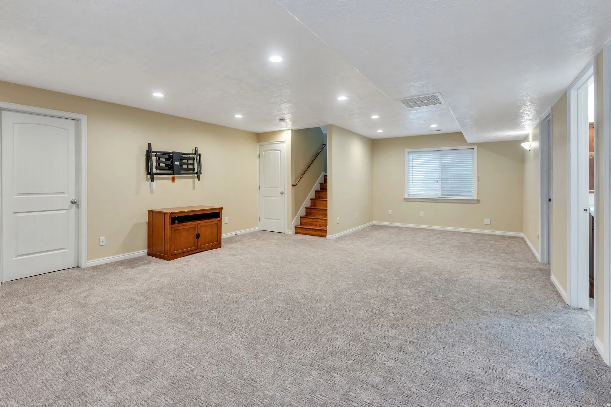 Recessed lighting, wood-finish staircase, light-toned carpeting, and neutral wall paint