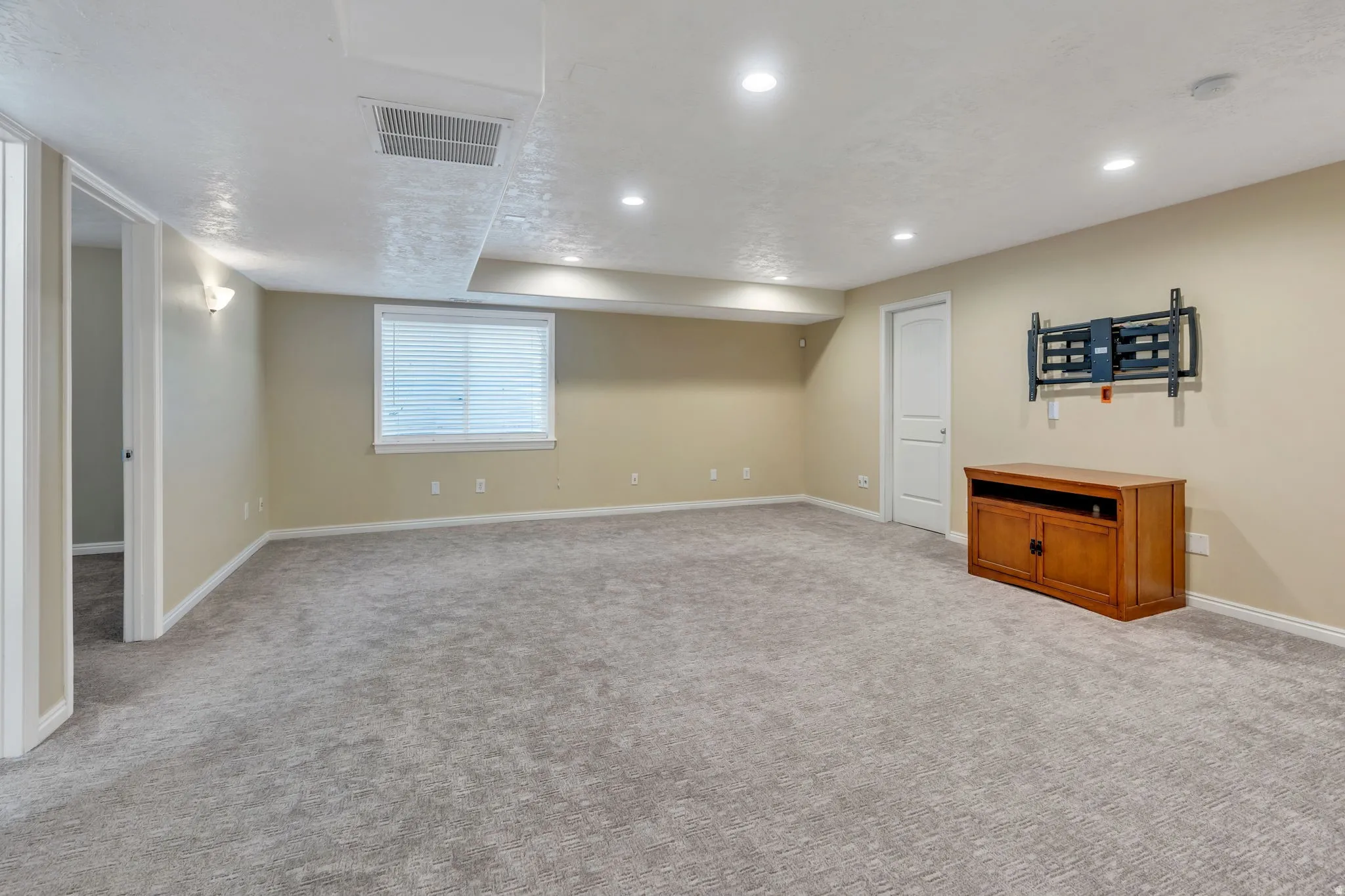 Recessed lighting illuminates the carpeted flooring and light-toned walls