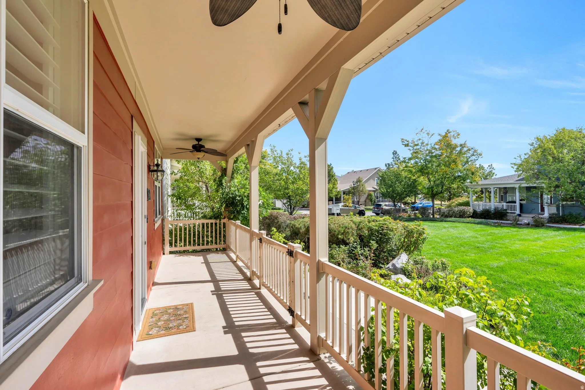 Covered front porch with a ceiling fan, white baluster railing, and exterior wall sconce