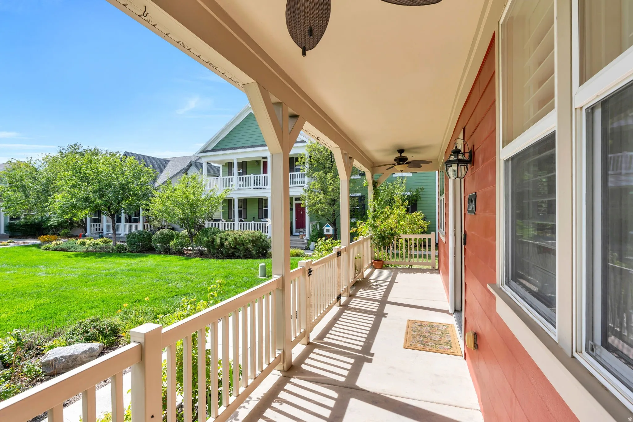 Covered front porch with two outdoor ceiling fans, white railing, and exterior wall lanterns