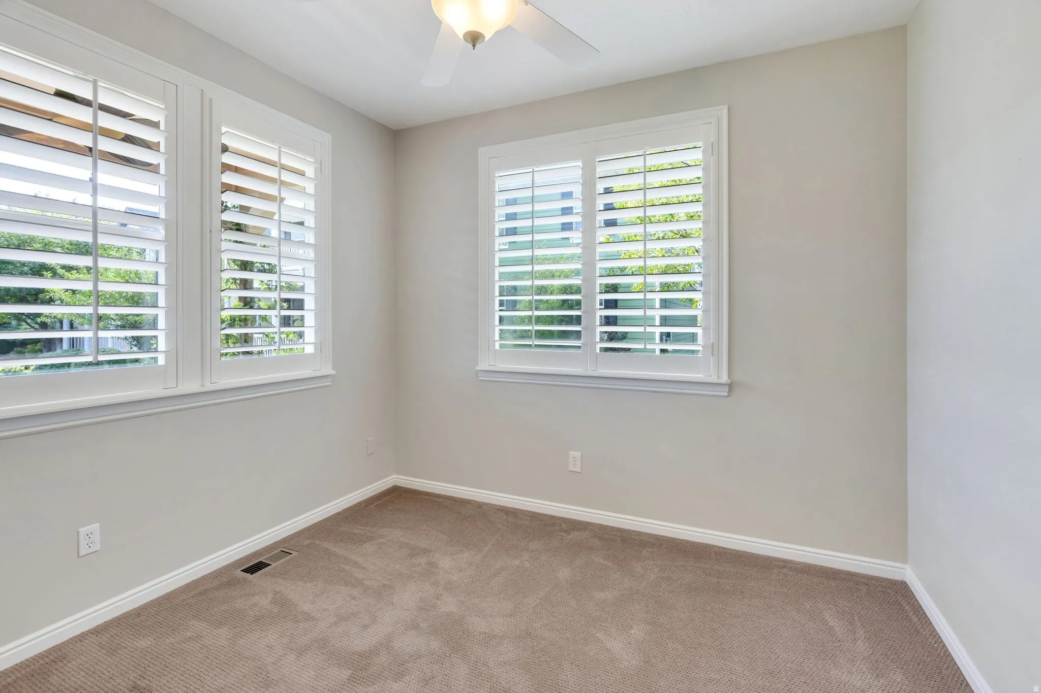 Multiple windows featuring plantation shutters, neutral wall color, and a ceiling fan with integrated lighting