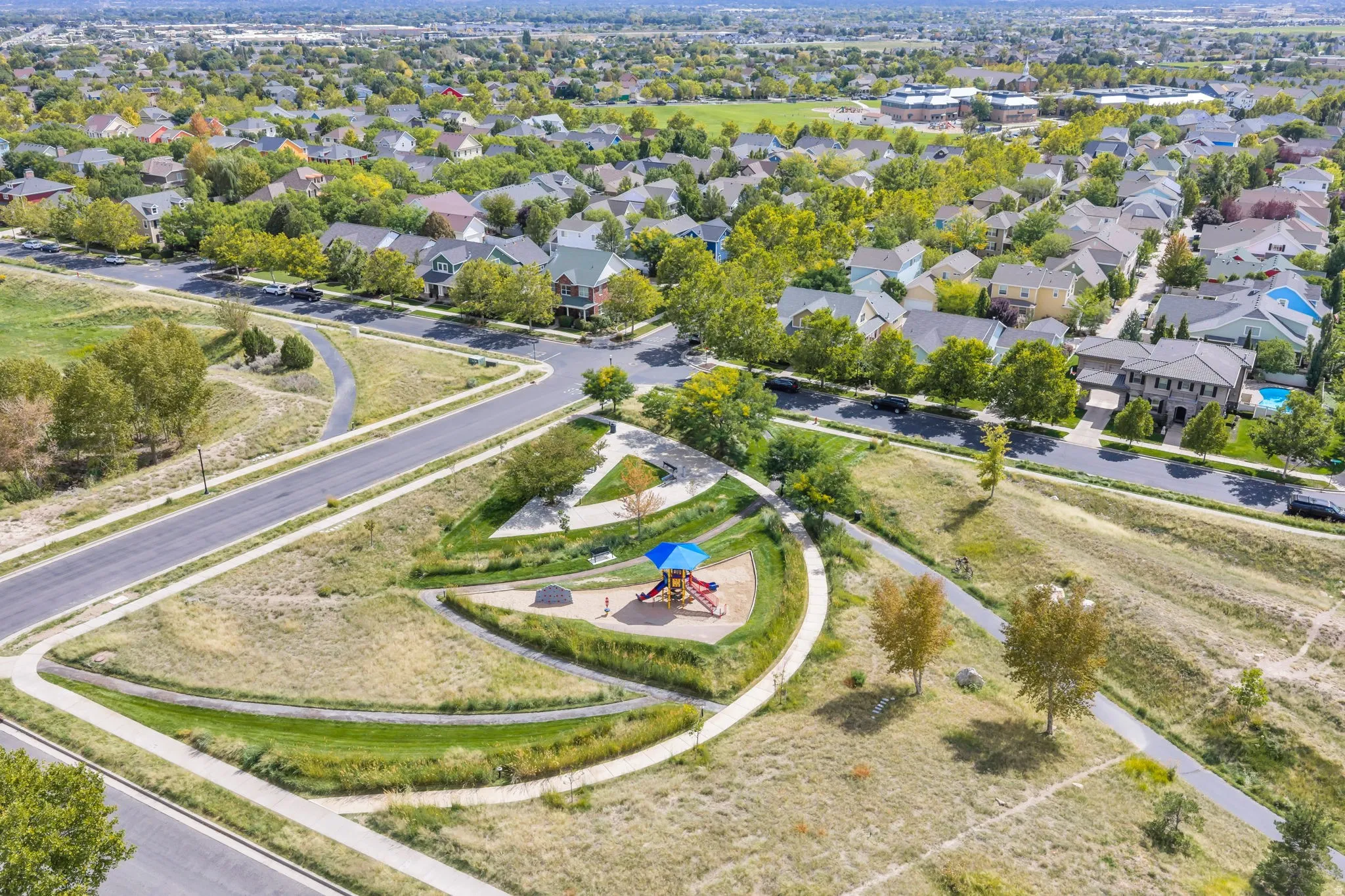 Neighborhood setting featuring mature trees, paved streets, a community park with playground equipment, and residential homes