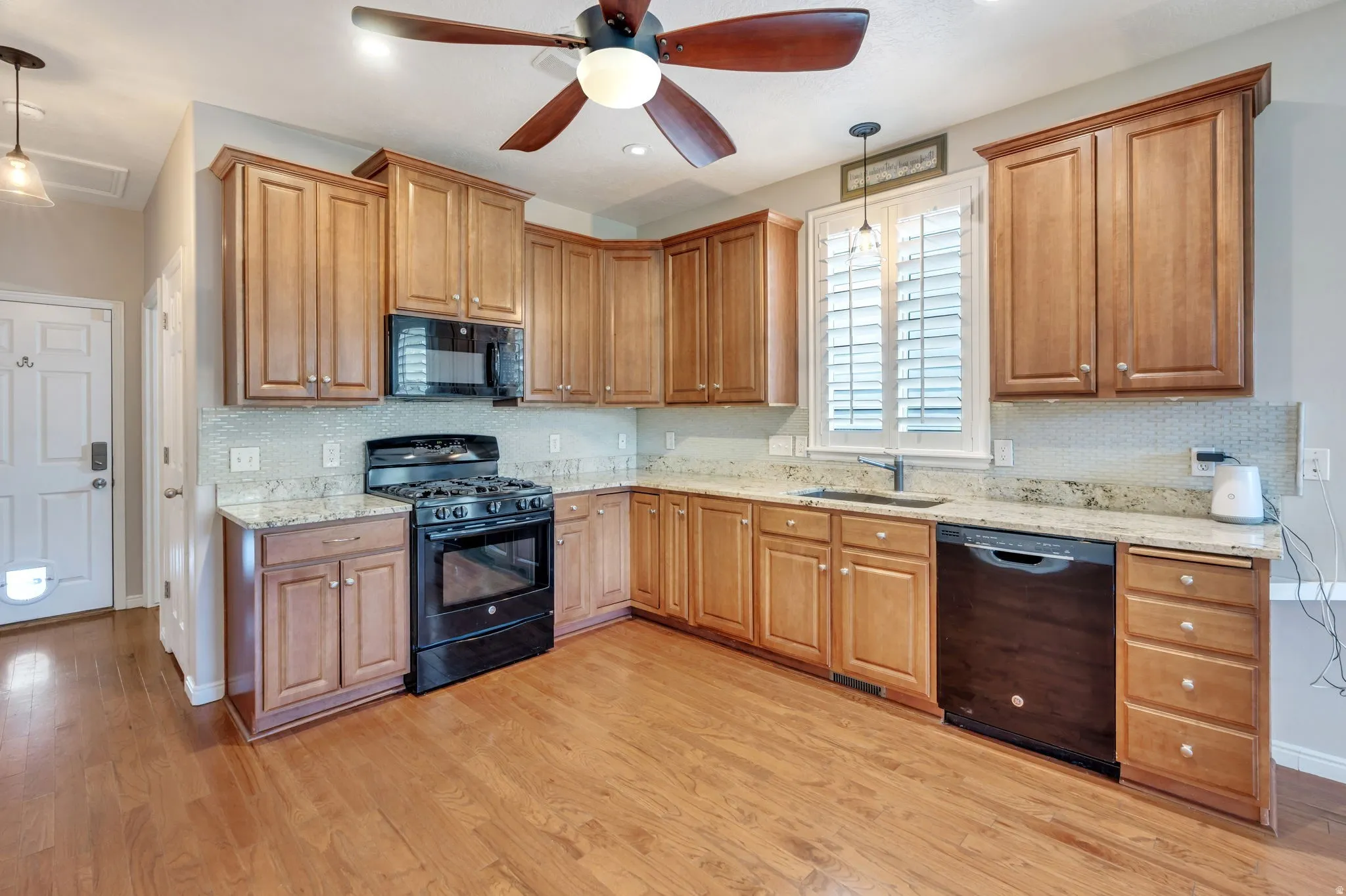 Kitchen featuring wood-finish flooring, wood cabinetry, stone countertops, a tile backsplash, and a ceiling fan with integrated lighting