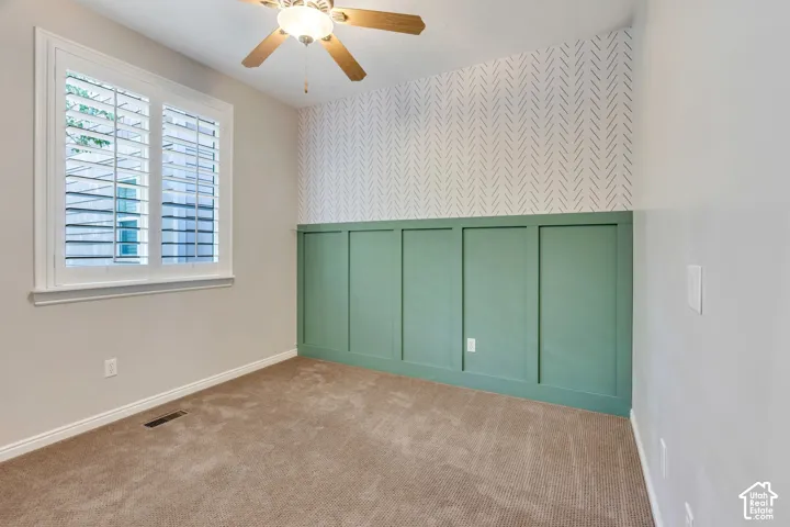 Window with interior plantation shutters, wood-finish ceiling fan, full wall paneling, patterned accent wall, and carpet flooring