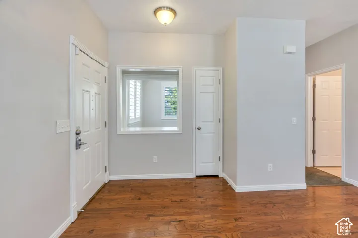 Entryway featuring wood-finish flooring, white paneled doors, and a decorative interior window with plantation shutters