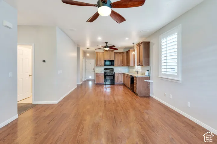 Open-concept living space featuring wood-finish flooring, recessed lighting, ceiling fans, and a kitchen with wood cabinetry and black appliances