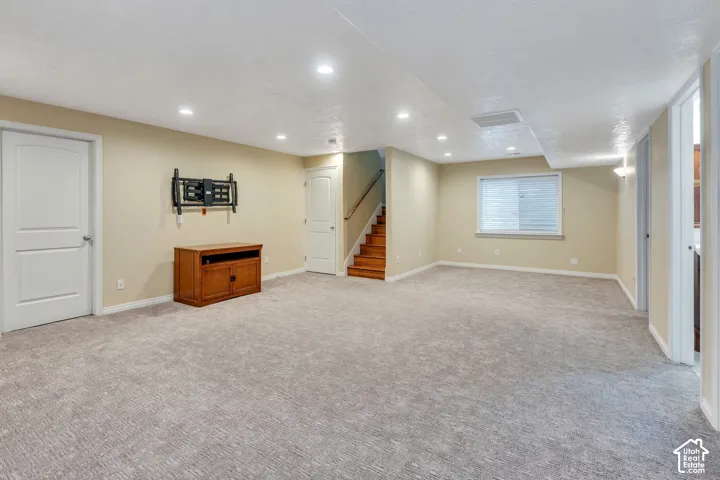 Recessed lighting, wood-finish staircase, light-toned carpeting, and neutral wall paint