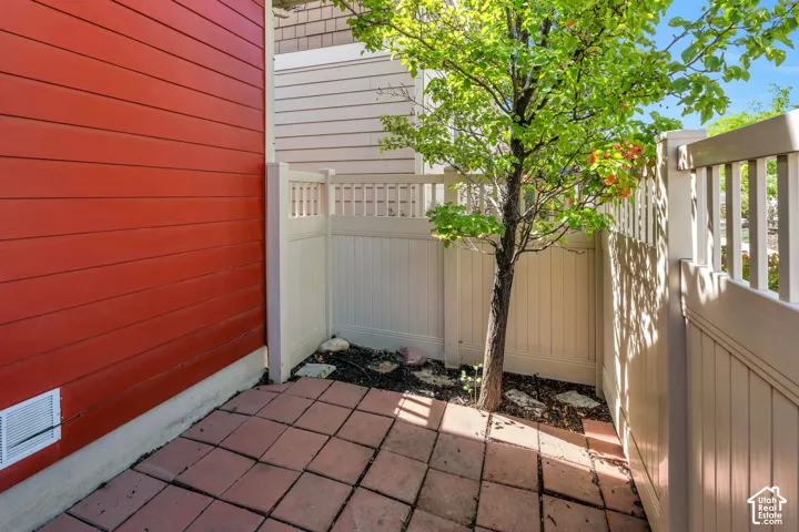 Paved patio area, contrasting red and beige siding, white privacy fencing, and a small tree