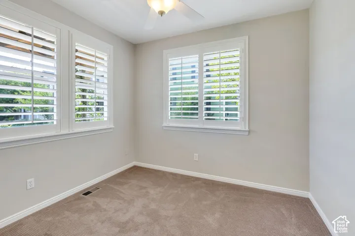 Multiple windows featuring plantation shutters, neutral wall color, and a ceiling fan with integrated lighting