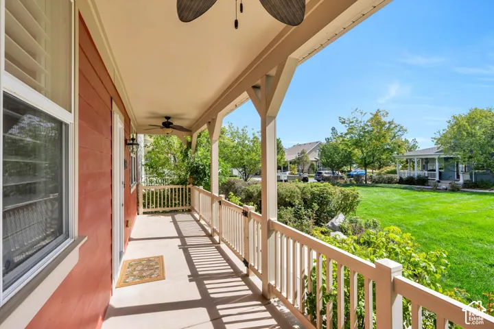 Covered front porch with a ceiling fan, white baluster railing, and exterior wall sconce