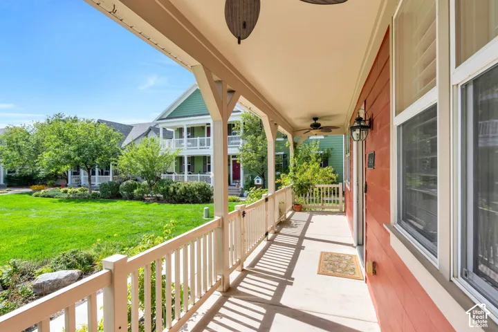 Covered front porch with two outdoor ceiling fans, white railing, and exterior wall lanterns