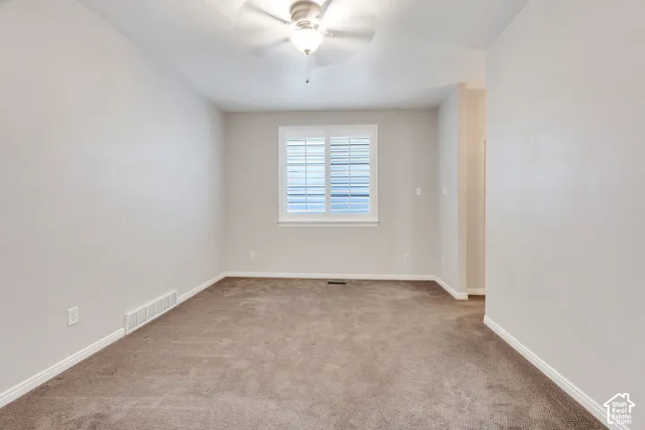 Neutral tone wall paint, textured ceiling, ceiling fan with integrated lighting, window with plantation shutters, and carpet flooring
