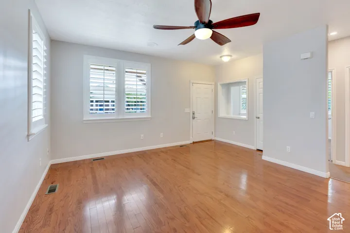 Spacious room featuring wood-finish flooring, white plantation shutters, a ceiling fan with integrated lighting, and recessed ceiling lights