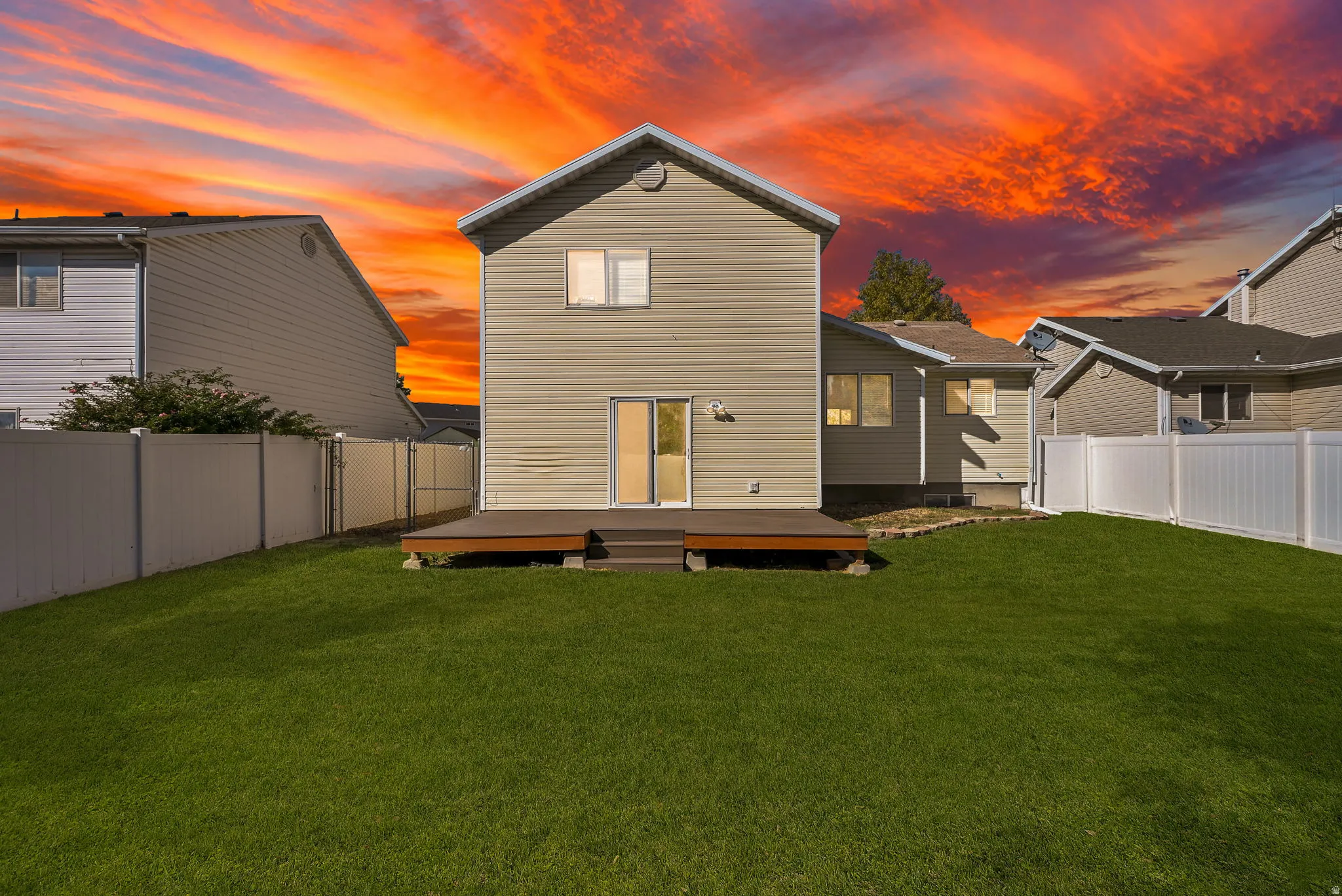 Expansive backyard featuring a manicured lawn, a wood-finish deck, and sliding glass door access to the interior