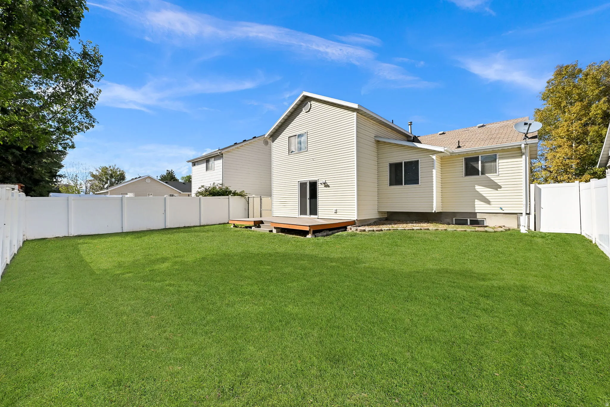 Expansive backyard featuring a manicured lawn, full perimeter privacy fencing, and a wooden deck