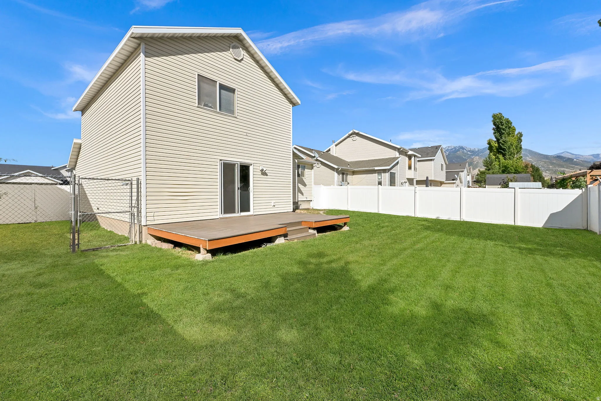 Expansive backyard featuring a manicured lawn, a low-profile wood deck, and a white privacy fence