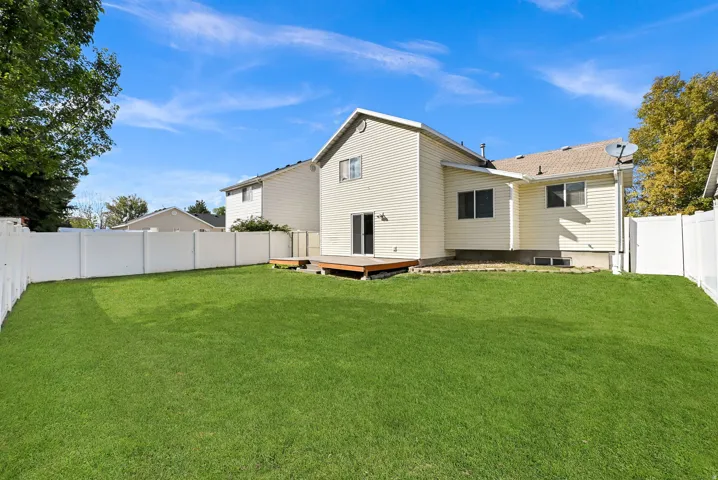 Expansive backyard featuring a manicured lawn, full perimeter privacy fencing, and a wooden deck