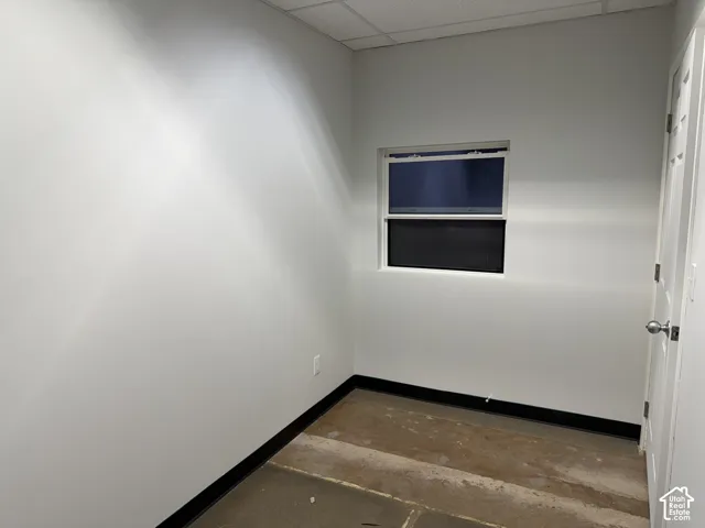 Interior room featuring neutral wall paint, a single-hung window, a drop ceiling, and a paneled door with metal hardware