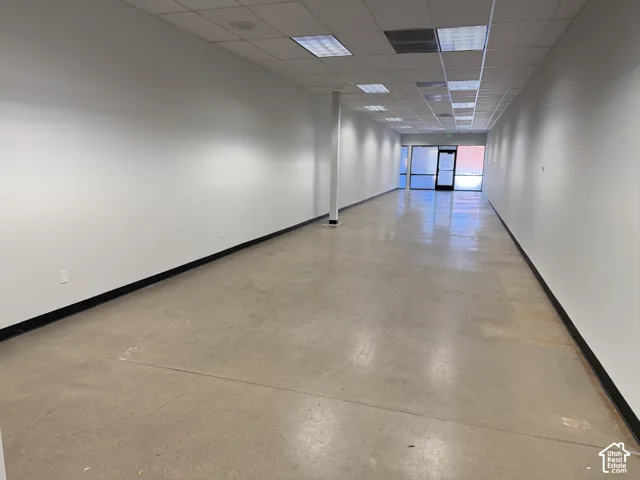 Open-concept interior featuring smooth concrete flooring, neutral painted walls, dropped ceiling grid, and an glass-panel exterior entry door