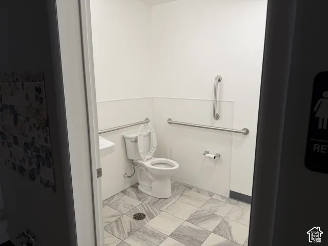 Restroom featuring tile flooring, a wall-mounted sink, a porcelain toilet, and stainless steel grab bars
