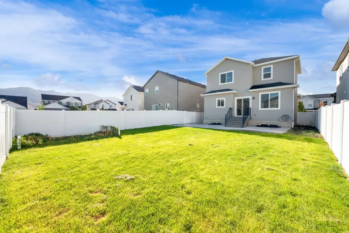Expansive backyard featuring a manicured lawn, full vinyl privacy fencing, a concrete patio, and a two-story exterior with multiple windows